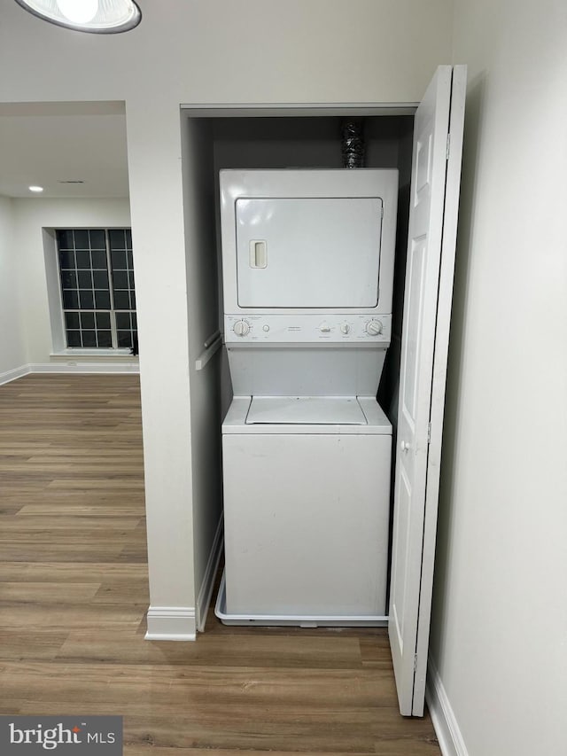 laundry area featuring baseboards, stacked washer and dryer, wood finished floors, and laundry area