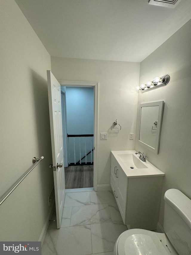 half bathroom featuring toilet, baseboards, marble finish floor, and vanity