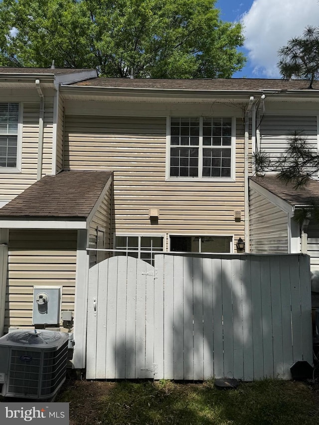 rear view of house with fence, central AC unit, and roof with shingles