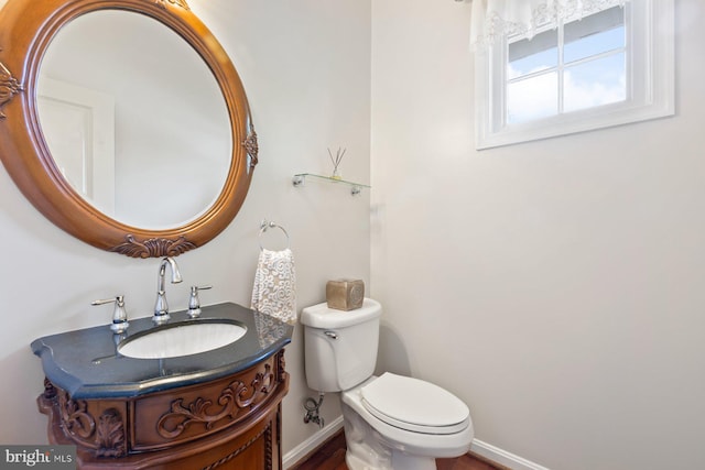 half bath featuring vanity, toilet, and baseboards