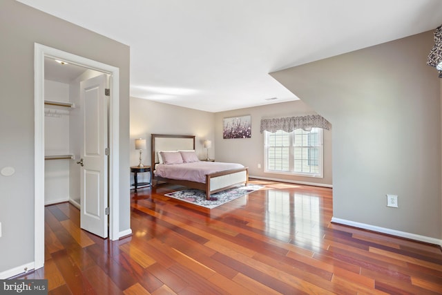 bedroom featuring wood-type flooring, a spacious closet, and baseboards