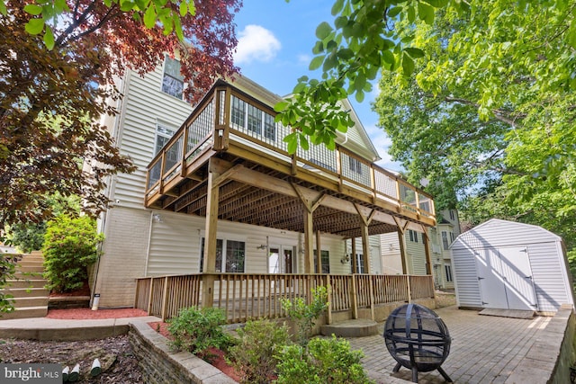 back of house with a fire pit, a shed, a wooden deck, an outbuilding, and a patio