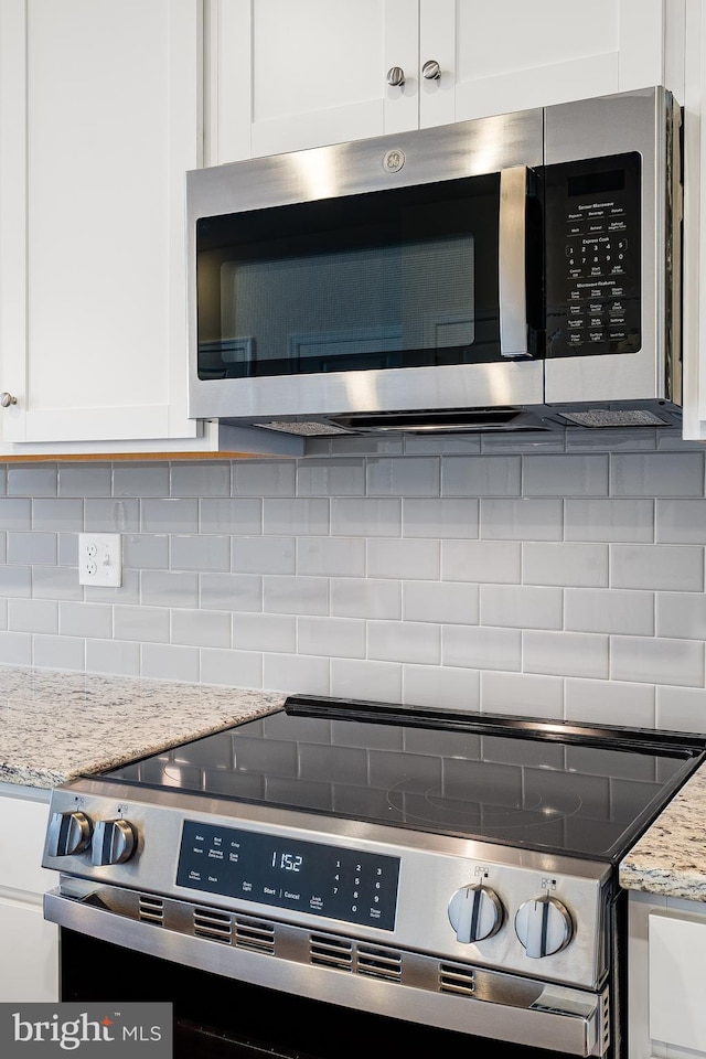 room details featuring appliances with stainless steel finishes, decorative backsplash, light stone counters, and white cabinets
