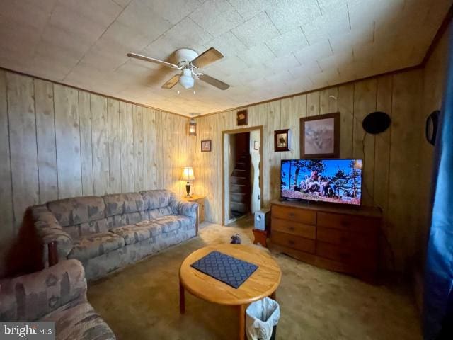 carpeted living room featuring wooden walls and ceiling fan
