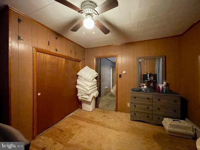 bedroom with ceiling fan, wood walls, carpet, and a closet