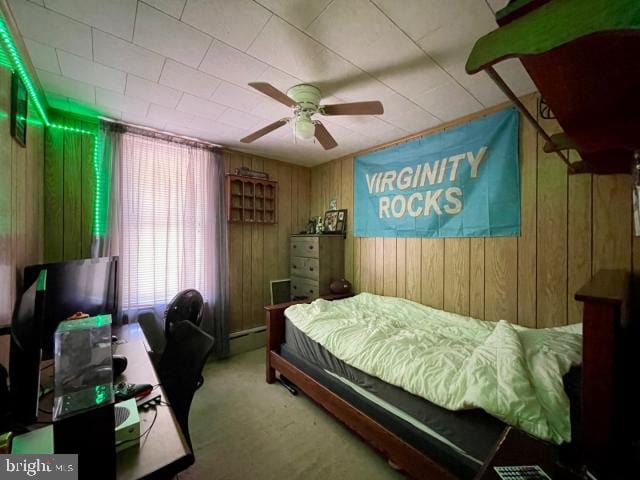 bedroom featuring wood walls, ceiling fan, carpet flooring, and baseboard heating