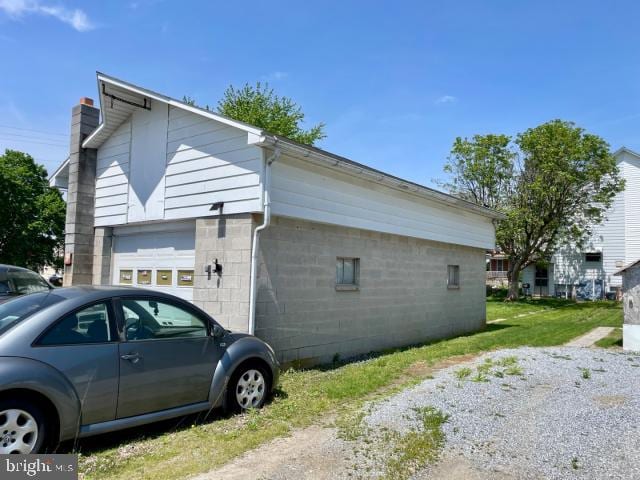 view of side of property featuring concrete block siding, a chimney, and an attached garage