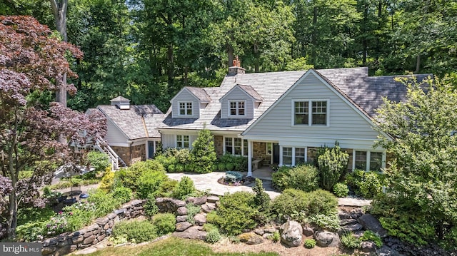 view of front facade with stone siding, a chimney, and a patio