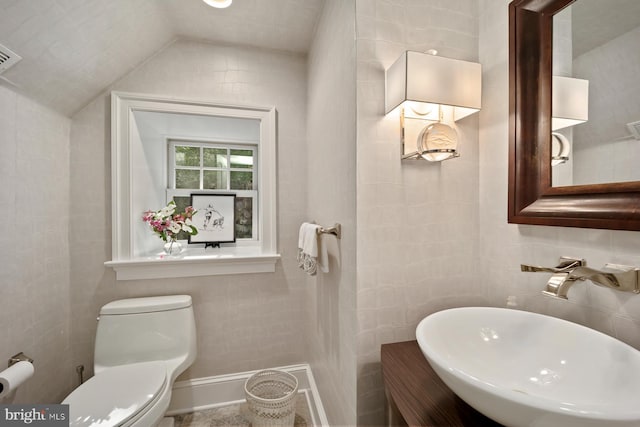 bathroom featuring a sink, toilet, lofted ceiling, and tile walls