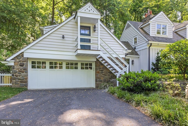 view of front of house with driveway, a chimney, a garage, stone siding, and stairs