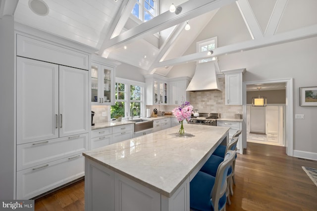 kitchen with a sink, custom range hood, white cabinets, stove, and beam ceiling
