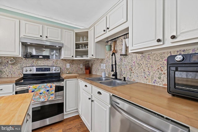 kitchen featuring stainless steel appliances, butcher block counters, a sink, wallpapered walls, and white cabinetry