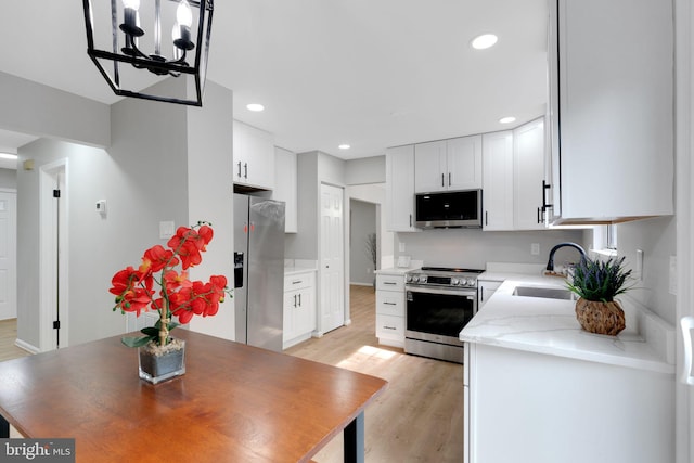 kitchen with light wood-type flooring, a sink, an inviting chandelier, stainless steel appliances, and white cabinetry