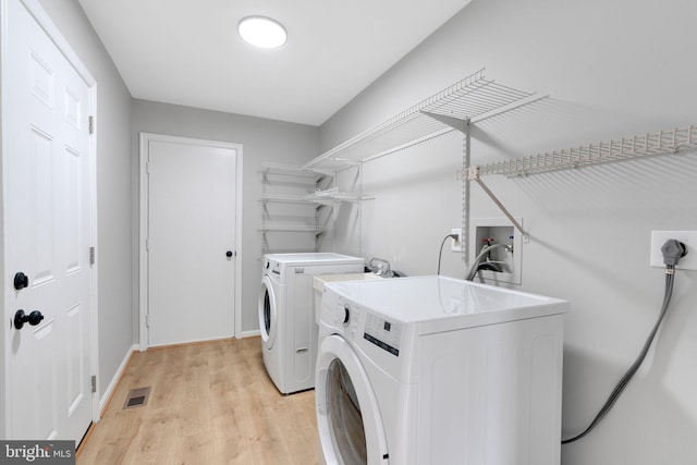 clothes washing area featuring visible vents, laundry area, baseboards, washer and clothes dryer, and light wood-style flooring