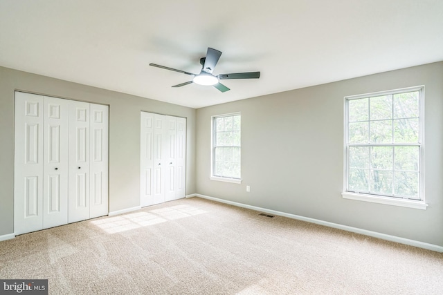 unfurnished bedroom with two closets, baseboards, and carpet flooring
