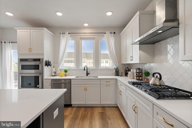 17303 Turnstone Dr, Dumfries, VA 22026 - kitchen with wall chimney exhaust hood, a sink, stainless steel appliances, white cabinets, and light wood-style flooring