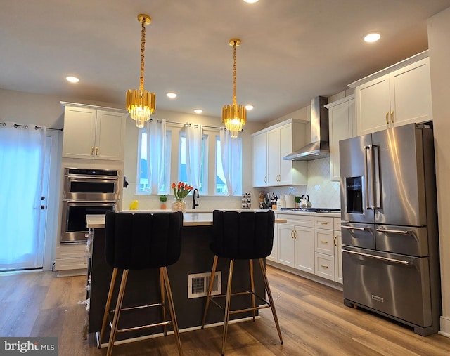 17303 Turnstone Dr, Dumfries, VA 22026 - kitchen with stainless steel appliances, wall chimney exhaust hood, white cabinets, a chandelier, and tasteful backsplash