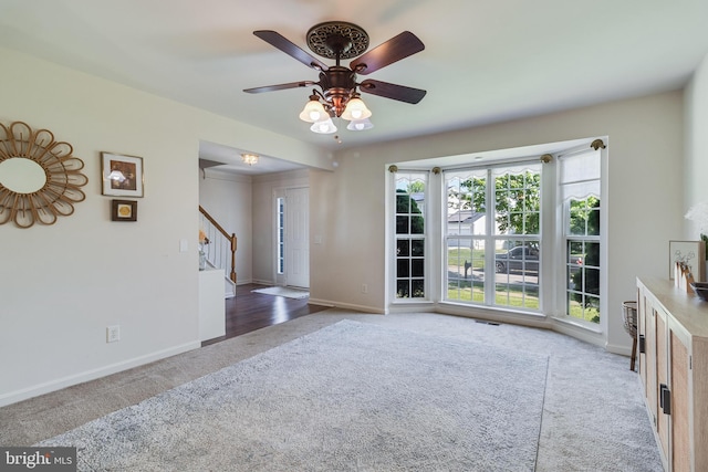 unfurnished living room featuring a ceiling fan, stairway, carpet floors, and baseboards