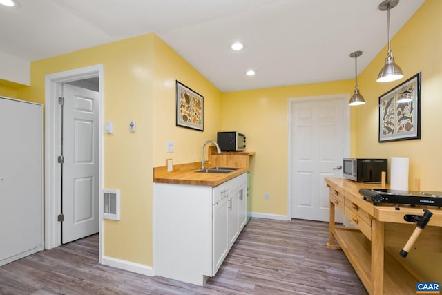 kitchen with a sink, recessed lighting, stainless steel microwave, wood finished floors, and butcher block counters