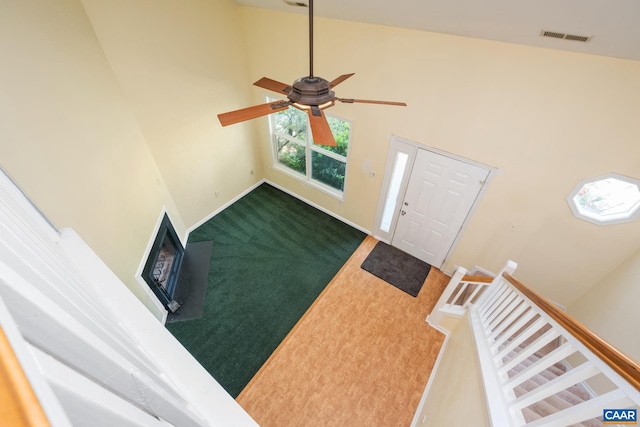 foyer with carpet, a ceiling fan, baseboards, a towering ceiling, and visible vents