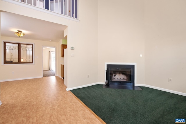unfurnished living room with a fireplace with flush hearth, baseboards, a high ceiling, and carpet flooring