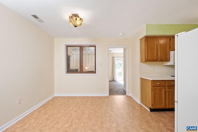 kitchen featuring visible vents, light countertops, brown cabinetry, and white appliances