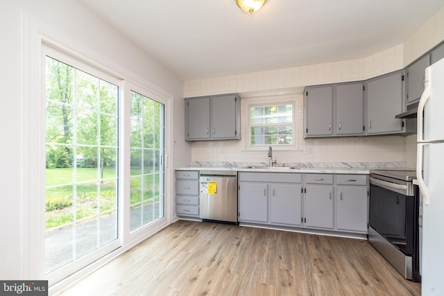 kitchen with a sink, light wood finished floors, stainless steel appliances, decorative backsplash, and gray cabinetry