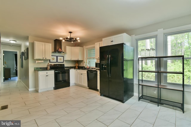 kitchen with black appliances, wall chimney range hood, dark countertops, a chandelier, and a sink