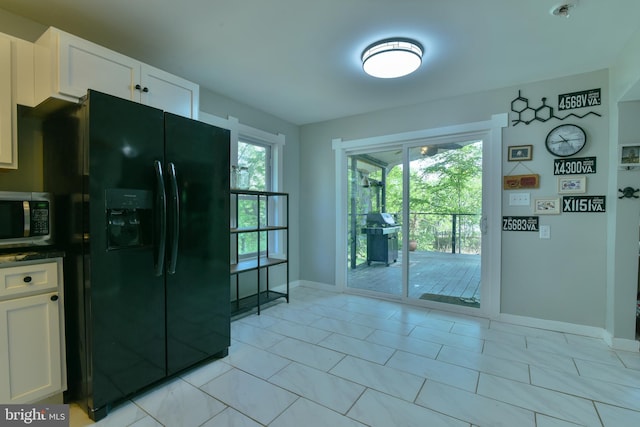 kitchen with black fridge, stainless steel microwave, baseboards, white cabinetry, and light tile patterned floors