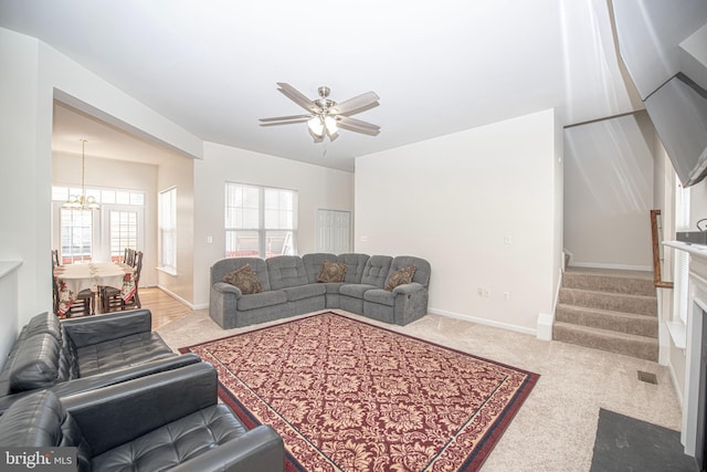 living area featuring stairway, baseboards, carpet, and ceiling fan with notable chandelier
