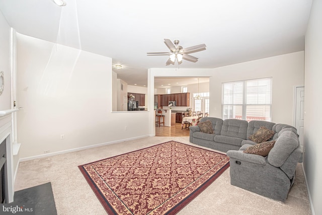 living area featuring a fireplace with flush hearth, baseboards, ceiling fan with notable chandelier, and carpet flooring