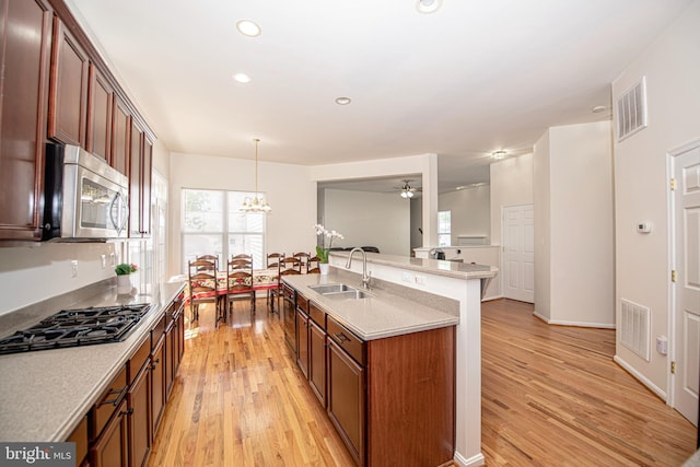 kitchen with a sink, light wood finished floors, stainless steel microwave, and black gas stovetop