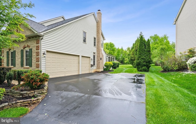 view of side of home with roof with shingles, brick siding, a chimney, a yard, and driveway