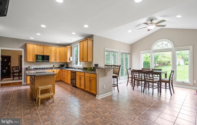 kitchen featuring dark countertops, stainless steel microwave, black dishwasher, and a breakfast bar