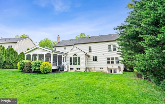 rear view of property featuring a sunroom, a yard, and a chimney