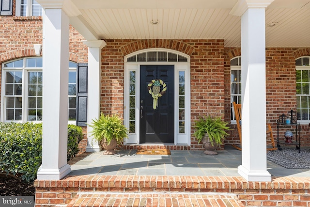 entrance to property with a porch and brick siding