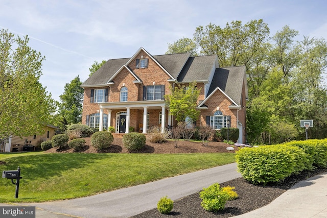 view of front facade with brick siding, roof with shingles, and a front yard