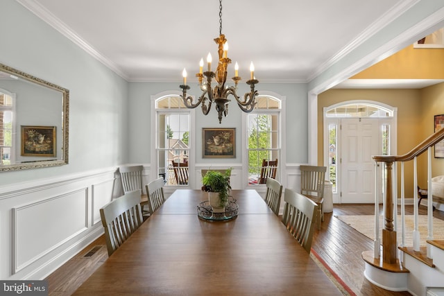 dining room with crown molding, an inviting chandelier, a decorative wall, a wainscoted wall, and wood finished floors