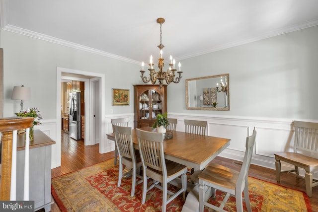 dining area featuring crown molding, wainscoting, wood finished floors, an inviting chandelier, and a decorative wall