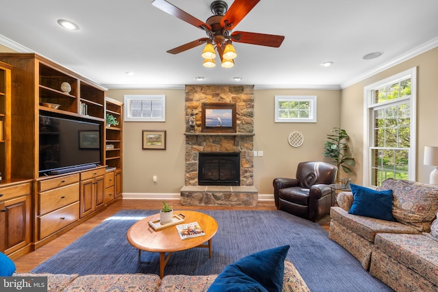 living room featuring crown molding, baseboards, a stone fireplace, ceiling fan, and light wood-style flooring
