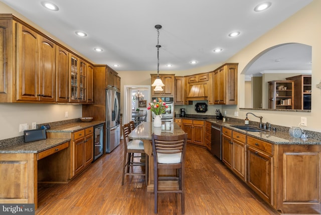 kitchen featuring brown cabinetry, appliances with stainless steel finishes, arched walkways, a sink, and wine cooler