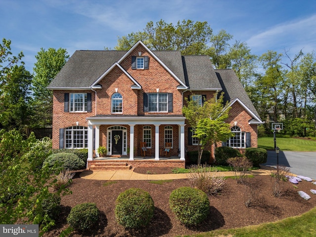 view of front facade with roof with shingles, a porch, and brick siding
