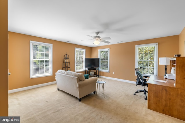 living area featuring baseboards, ceiling fan, a wealth of natural light, and light carpet