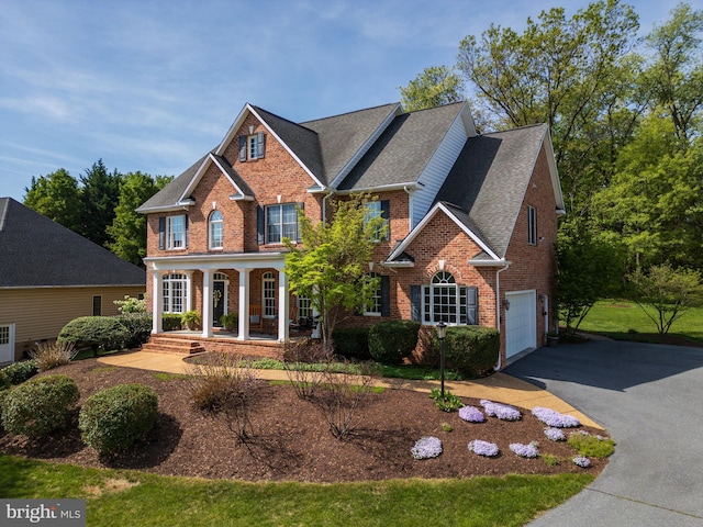 view of front of property featuring a garage, aphalt driveway, covered porch, brick siding, and a shingled roof