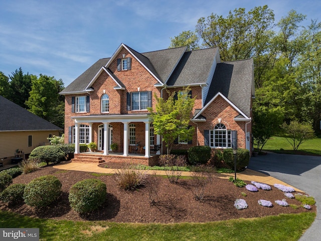 view of front of property featuring brick siding, roof with shingles, and a porch
