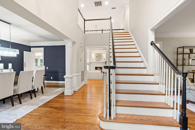 12019 Wandabury Rd, Oakton, VA 22124 - stairs with wood finished floors, crown molding, a towering ceiling, a chandelier, and a warm lit fireplace