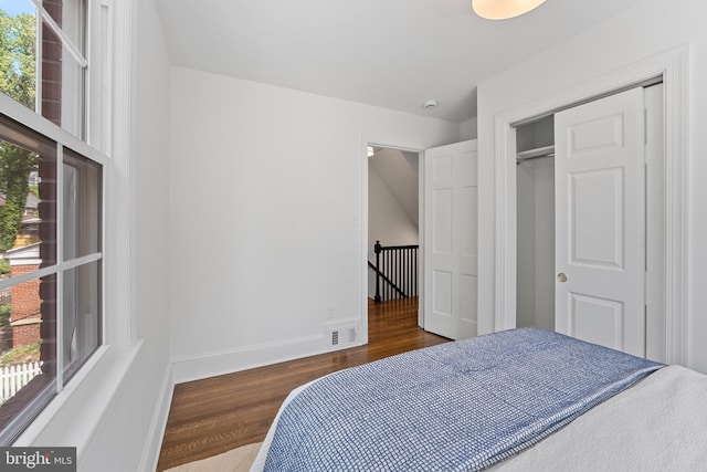 bedroom with baseboards, a closet, wood finished floors, and visible vents