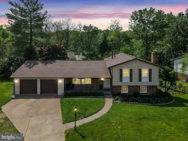 split level home featuring driveway, a chimney, brick siding, an attached garage, and a yard