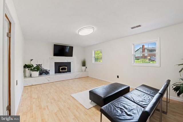 living area featuring a high end fireplace, baseboards, wood finished floors, and visible vents