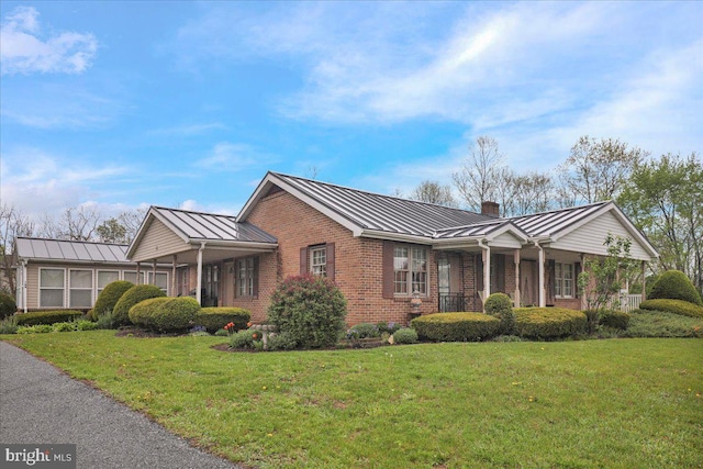 view of front of home featuring a front lawn, brick siding, a chimney, a standing seam roof, and metal roof